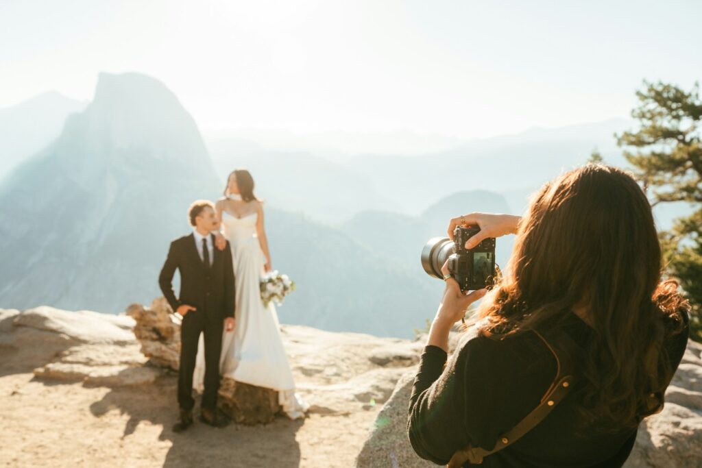 Bride and groom posing for photographer on mountain overlook.