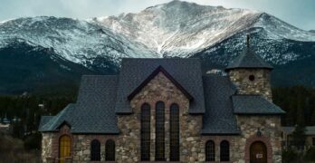 Beautiful stone chapel nestled against a snow-capped Rocky Mountain in Estes Park, Colorado.