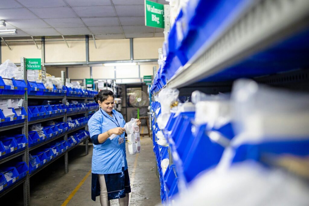 Female worker organizes shelves in a warehouse. Industrial setting with labeled storage bins.