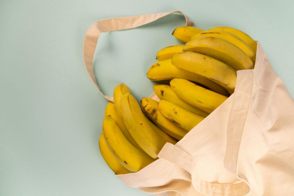 Fresh bananas in an eco-friendly canvas bag on a pastel background.