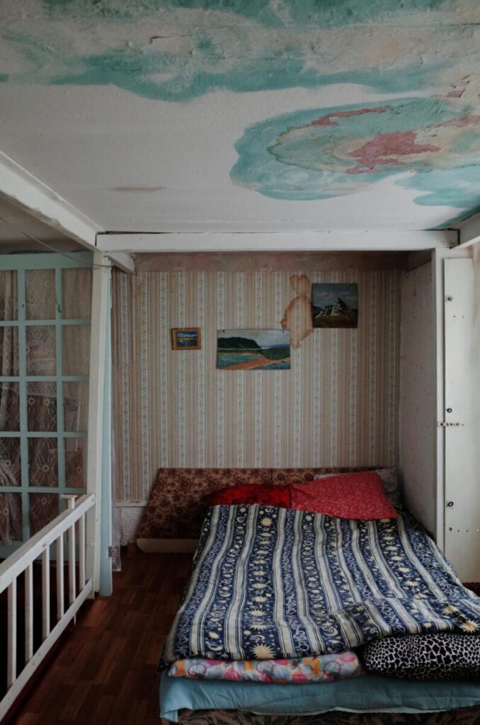 A small bedroom with a unique ceiling design, featuring water stains and an eclectic bed setup.