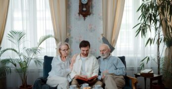 Elderly couple with son enjoying a photo album at home, sharing memories.