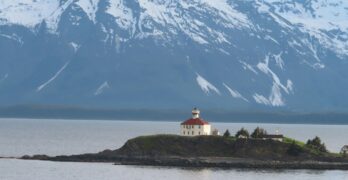 A lighthouse sits beneath snowy mountains.
