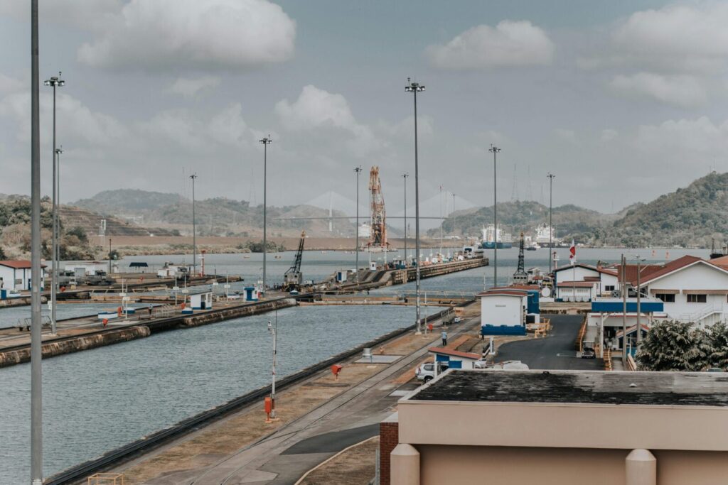 A panoramic daytime view of the Panama Canal locks with surrounding landscape and maritime infrastructure.