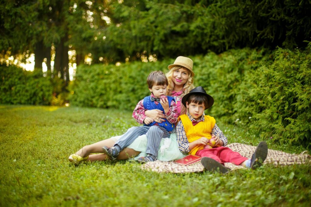 Mother and two sons relaxing on a blanket in a sunny park, enjoying a leisure summer afternoon.