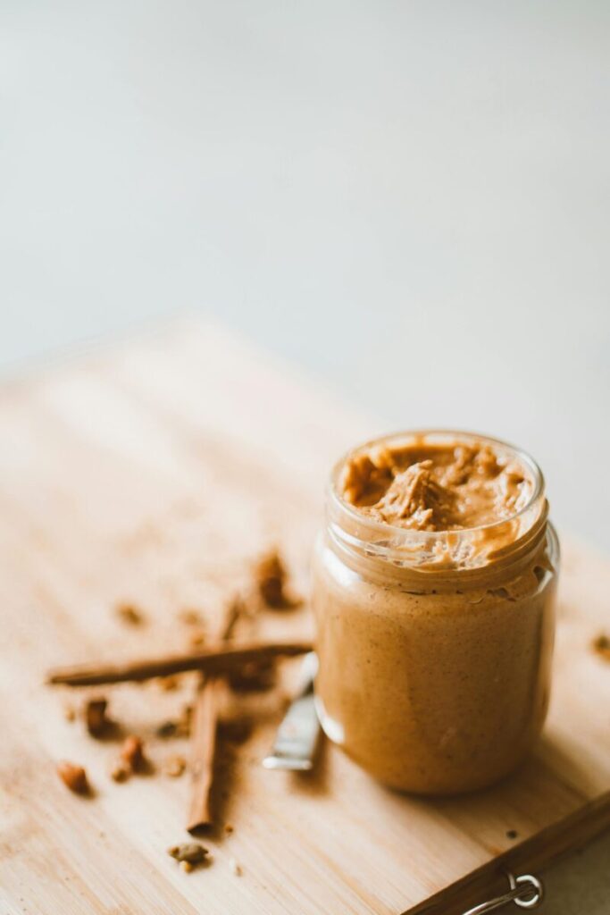Delicious homemade organic peanut butter in a glass jar on a wooden board.