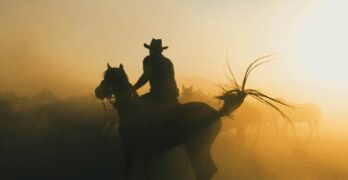 A cowboy riding a horse through a dusty sunrise, creating a dramatic silhouette.