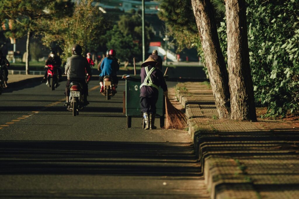 A street sweeper cleaning the roads in Dalat, Vietnam amid morning traffic.