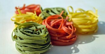Vibrant multicolored nests of raw pasta on a light surface, showcasing a variety of flavors.