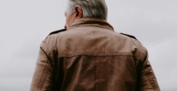 a man in a brown leather jacket standing on a beach