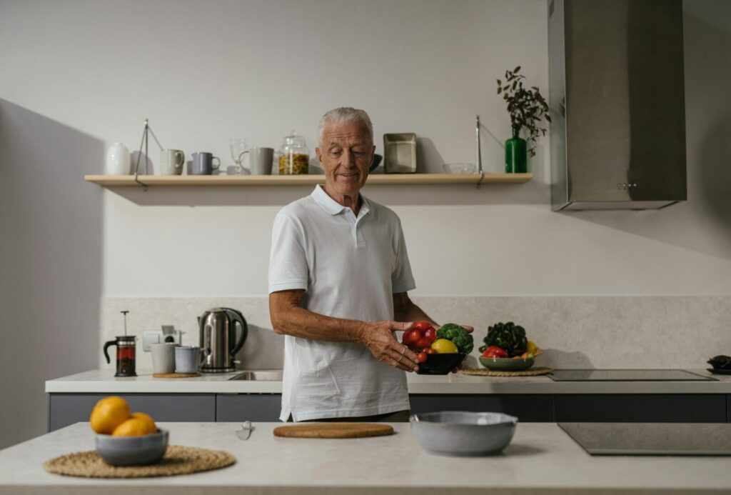 Elderly man joyfully prepares vegetables in a bright, contemporary kitchen setting.