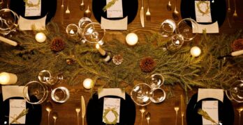 Elegant Christmas dinner table with candles, pine decor, and luxury dinnerware.