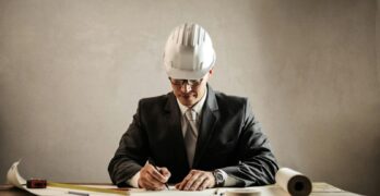 Engineer in a suit drafting architectural plans at a desk indoors.