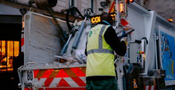 A garbage collector works on a city street, managing waste collection at dusk.