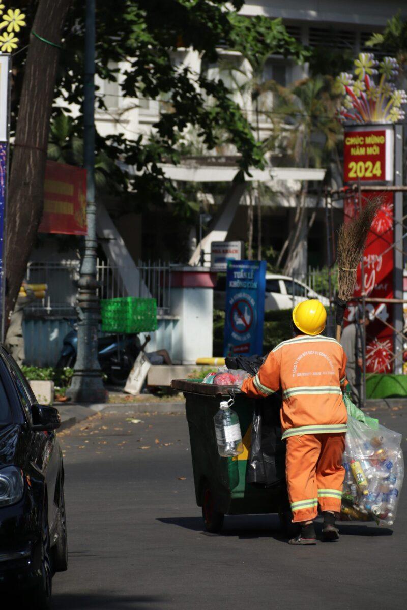 Back view of a city sanitation worker with safety gear managing waste in an urban setting.