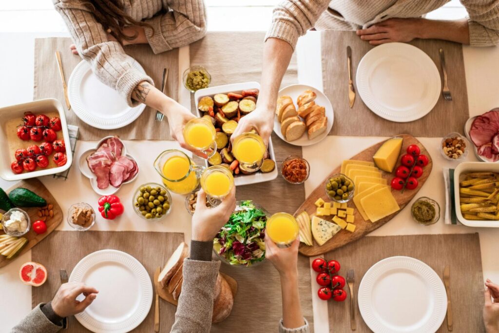 Top view of a family toasting at a lunch table with cheese, olives, and fresh salads.