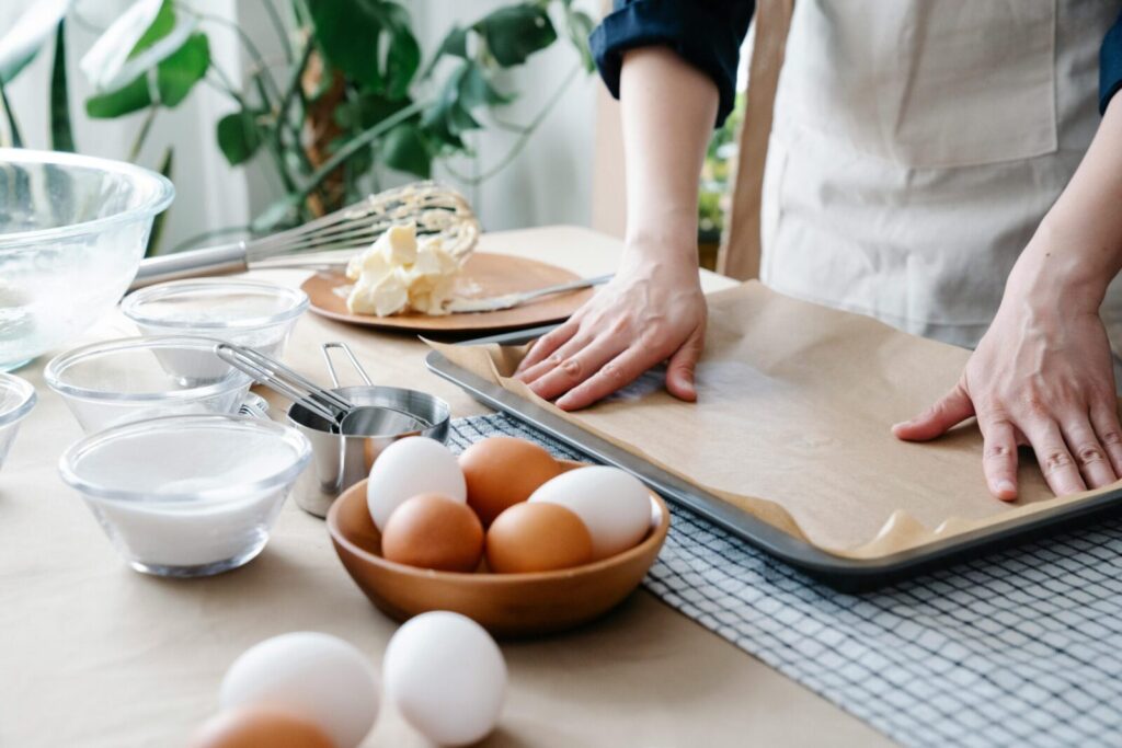 Hands preparing baking tray with ingredients ready for baking, including eggs and flour.