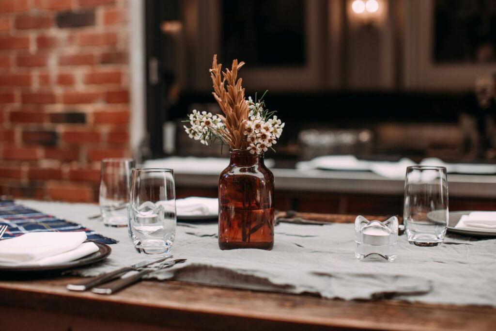 Charming rustic table setting with glassware, cutlery, and a floral centerpiece in an amber bottle.
