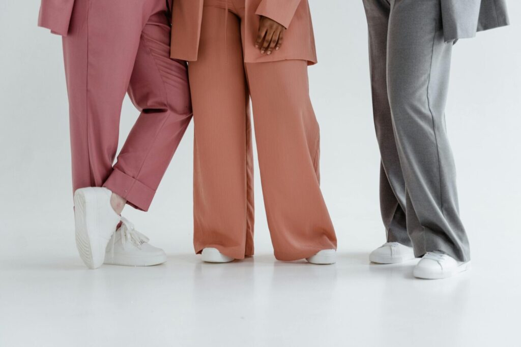 Three people wearing stylish wide-leg pants and white sneakers on a white background. Studio shot.