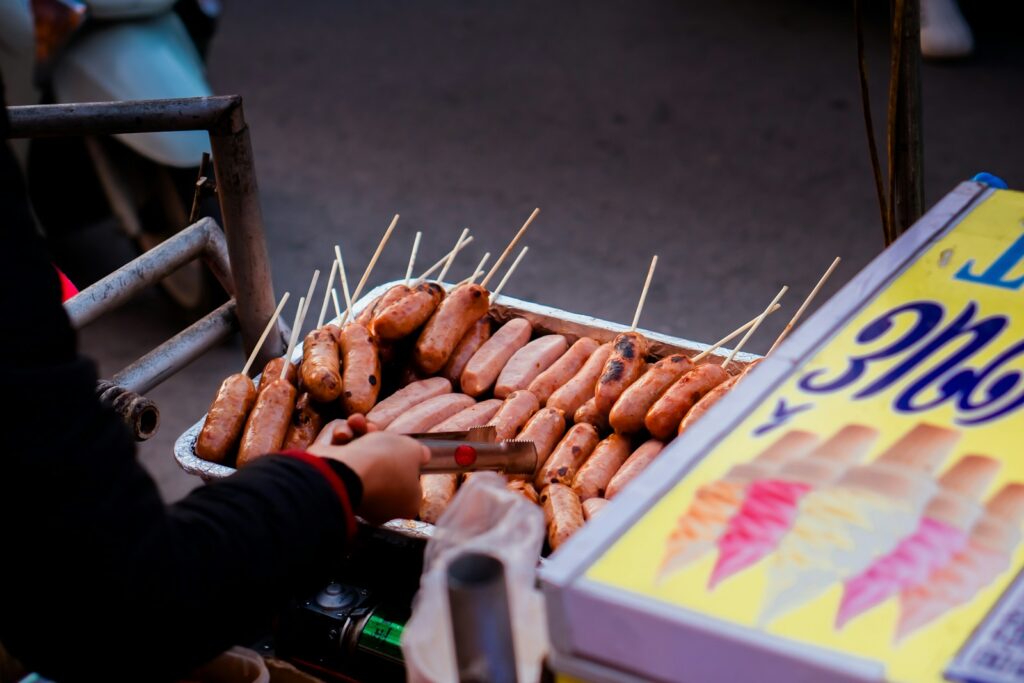 A person holding a tray of hot dogs on a stick