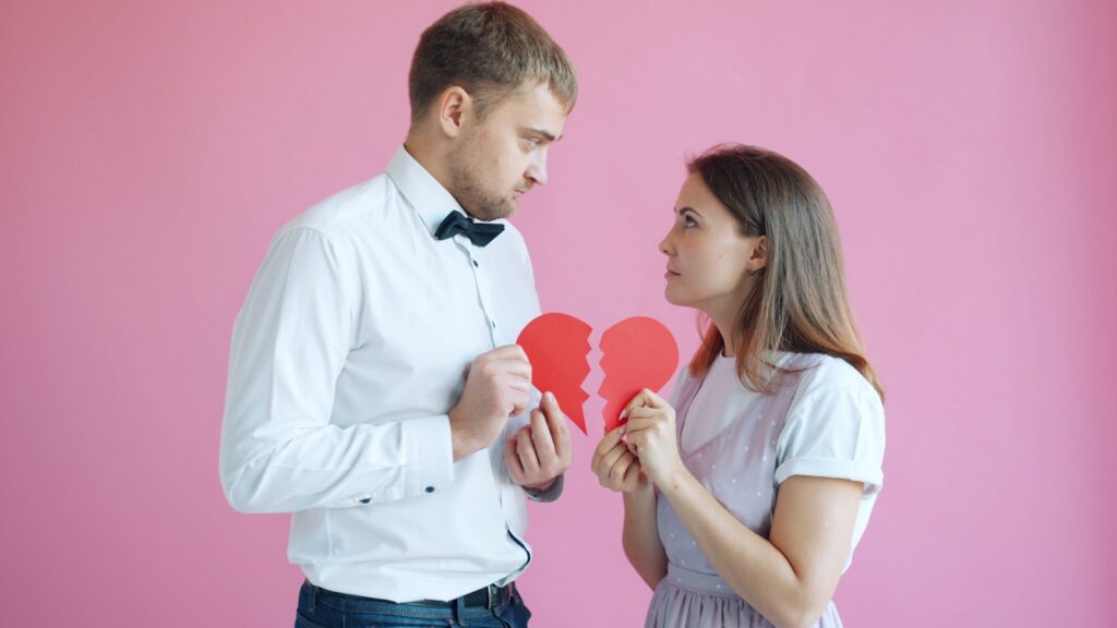 Couple holding broken heart halves on pink background