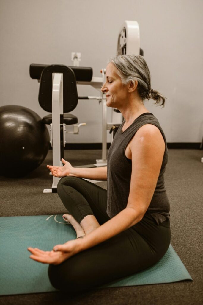 Elderly woman meditating on mat in gym, focusing on relaxation and mindfulness.