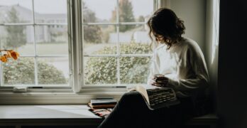 A woman sitting on a window sill reading a book