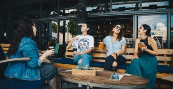 Four friends laughing and enjoying drinks together at an outdoor cafe setting, reflecting happiness and camaraderie.