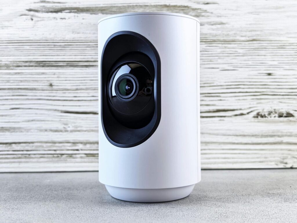 Stylish white home security camera placed on a wooden surface for indoor surveillance.