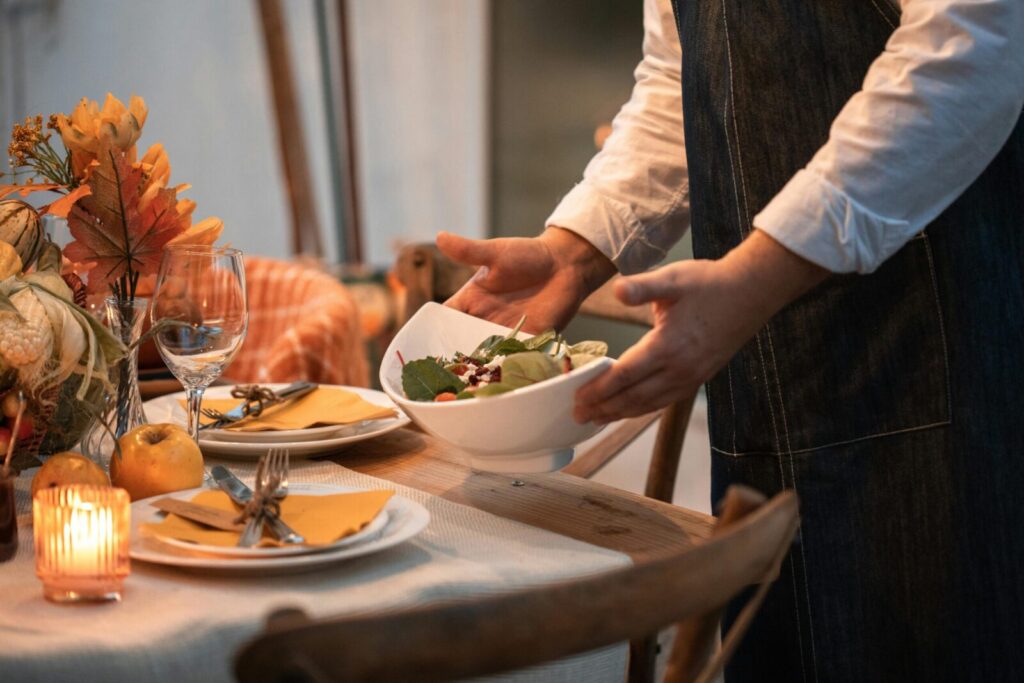 Warm and inviting autumn table setting with a person serving salad, perfect for Thanksgiving dinner.
