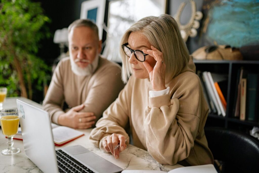 Elderly couple looking at laptop screen indoors, focused and engaged in a task.