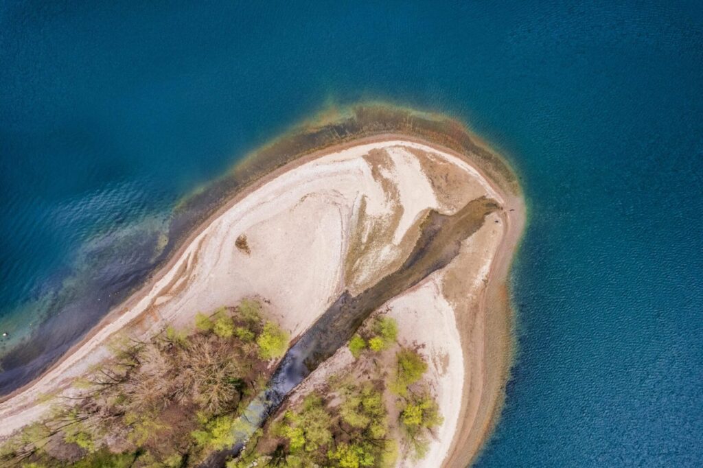 Aerial photograph of a small island with sandy beaches surrounded by a vivid blue lake.