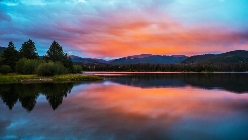 Tranquil sunset over Breckenridge lake with vivid sky and mountain reflections.