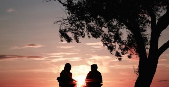 silhouette of two person sitting on chair near tree