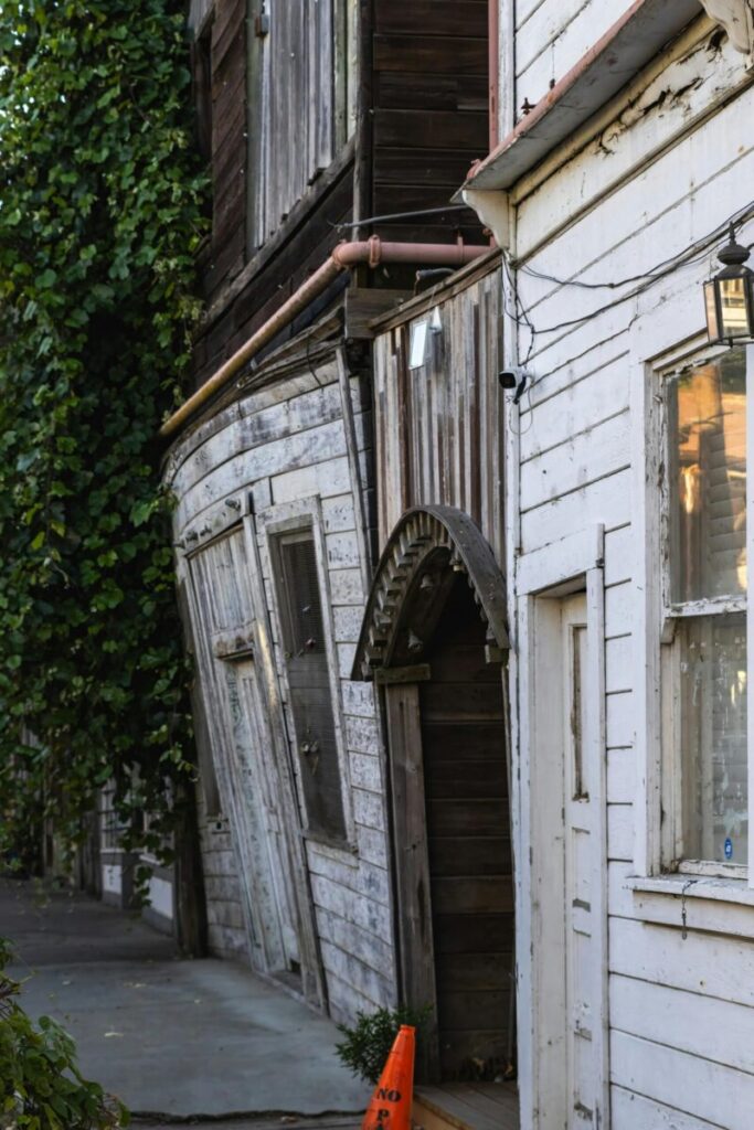 A vertical shot of derelict wooden houses with overgrown ivy and leaning walls in an urban environment.