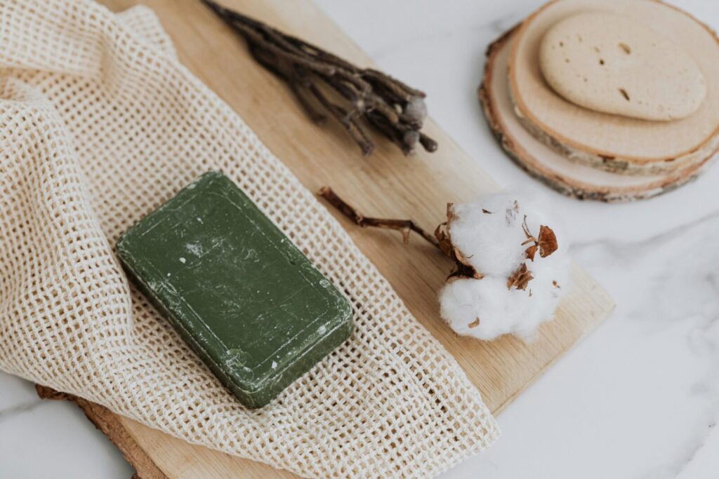 Natural green soap with cotton and loofah on wooden board promoting zero waste lifestyle.