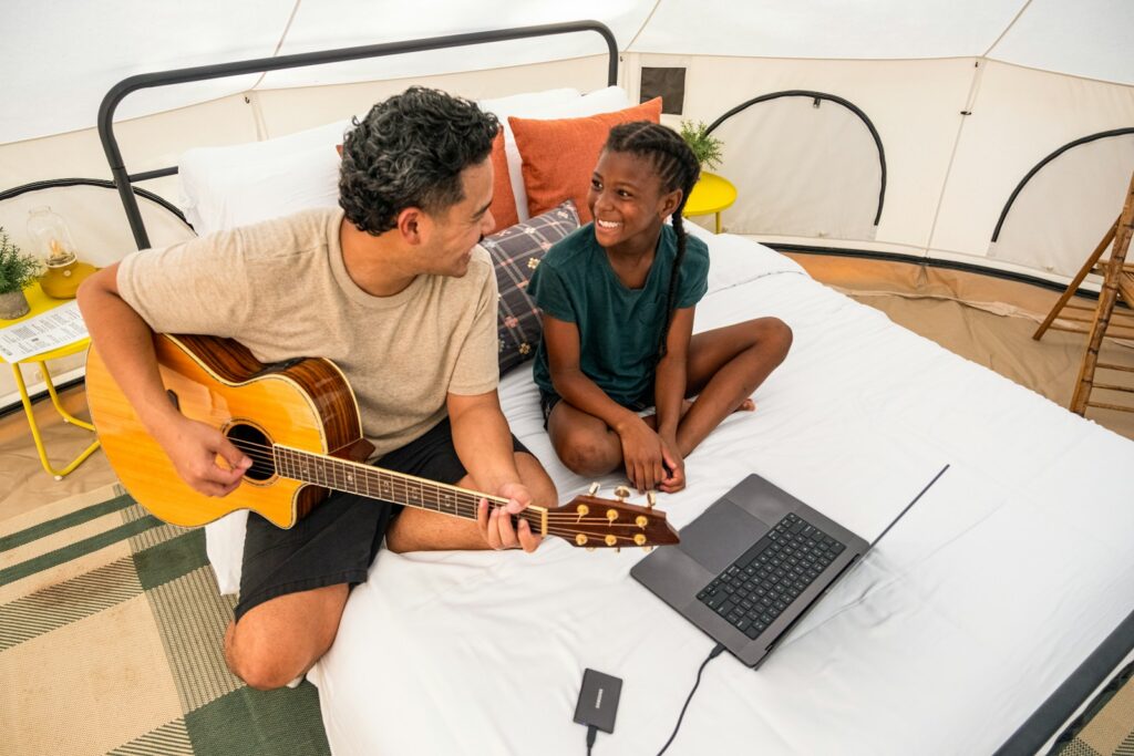 Man plays guitar for smiling girl on bed