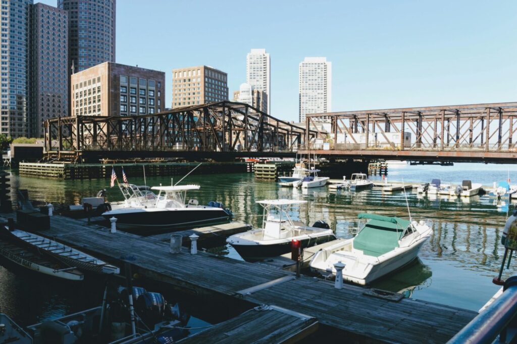 Scenic view of Boston's waterfront with boats, buildings, and a bridge on a sunny day.