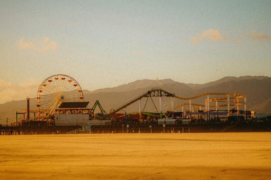 Scenic view of Santa Monica Pier with ferris wheel and roller coaster against mountain backdrop at dusk.