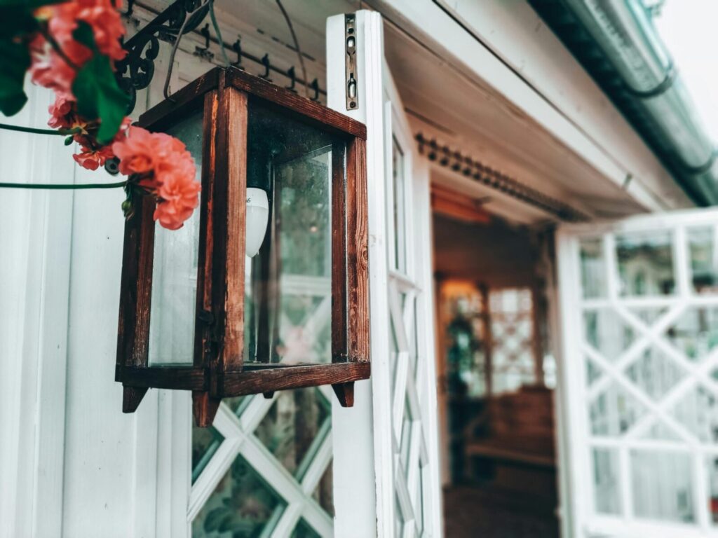 Close-up of a rustic wooden lantern with vibrant pink flowers at a house entrance.