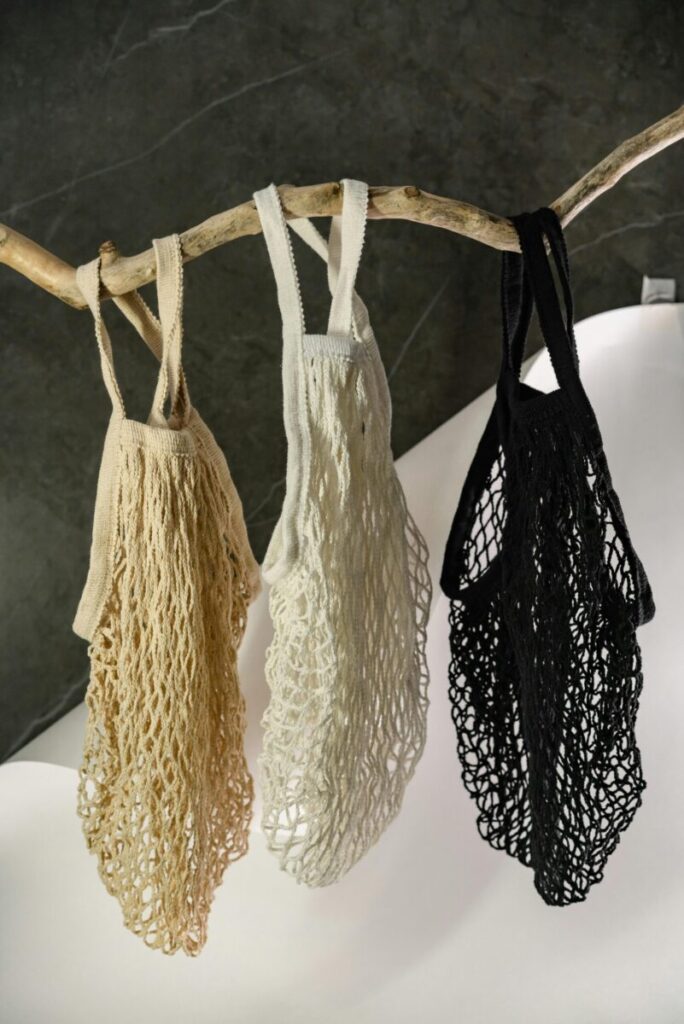 Three eco-friendly mesh bags in different colors hanging from a branch.