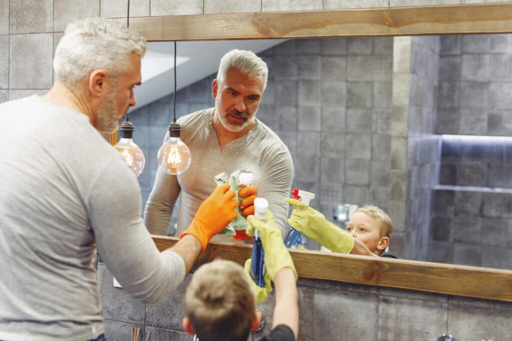 Father and son bonding over cleaning the bathroom mirror as part of their daily routine.