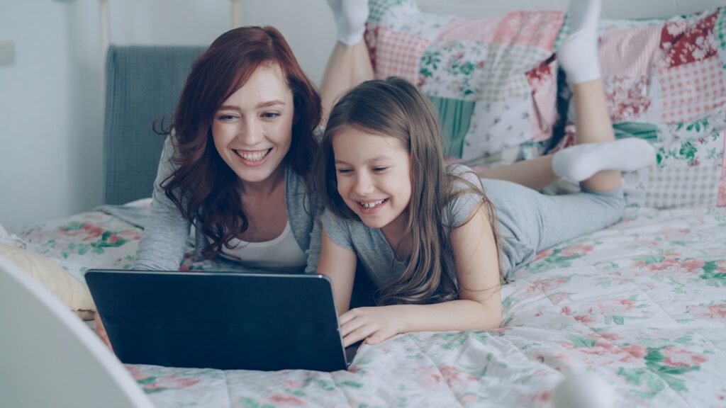 Mother and daughter laugh while using a laptop.