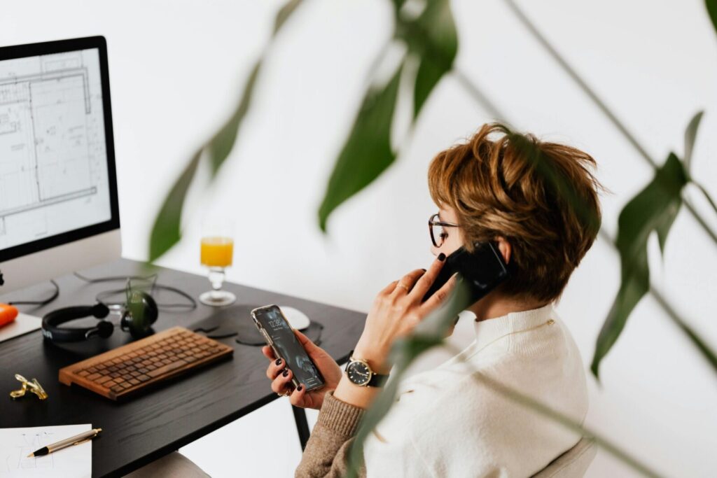 Side view of a woman multitasking in a modern office, using phone and computer.