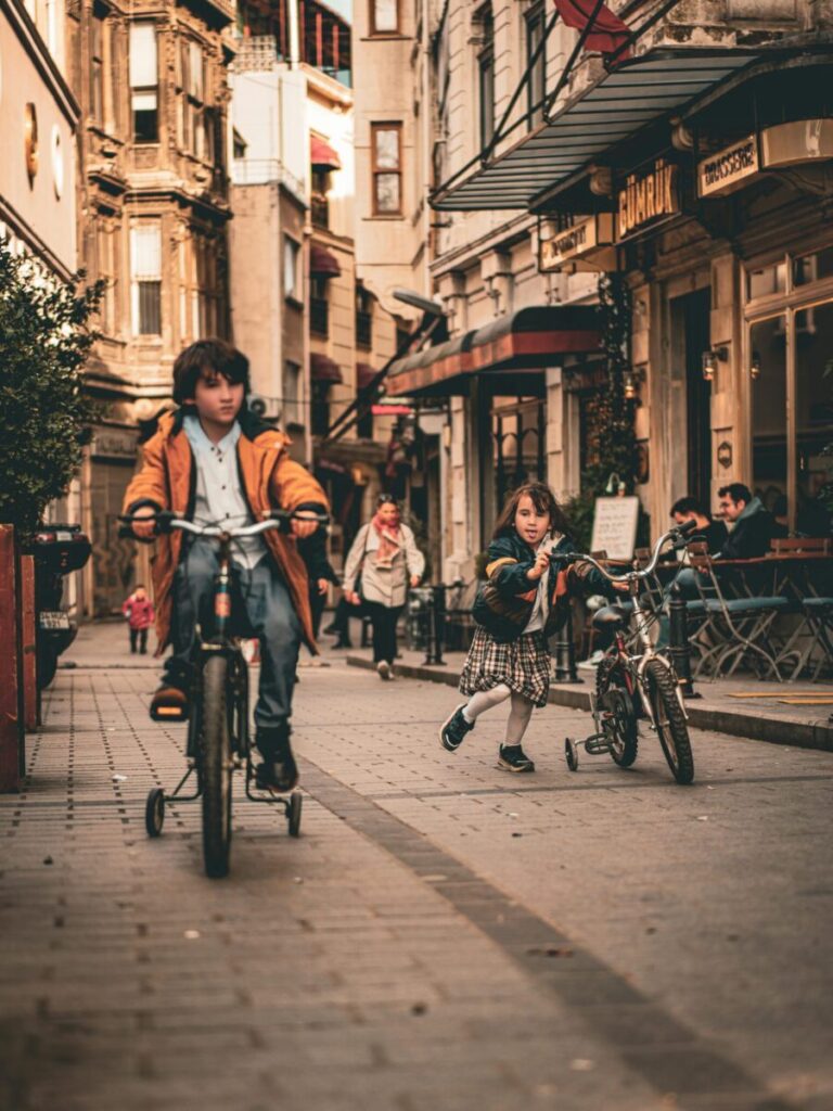 Kids enjoy a ride on bikes down a lively street filled with cafes and historic architecture.