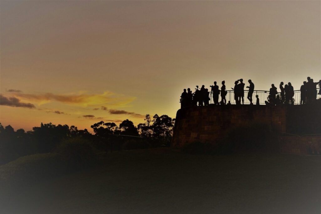 Silhouettes of people observing a vibrant sunset over Brisbane skyline, creating a peaceful and scenic atmosphere.