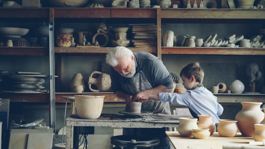 A potter teaches a boy how to work with clay.