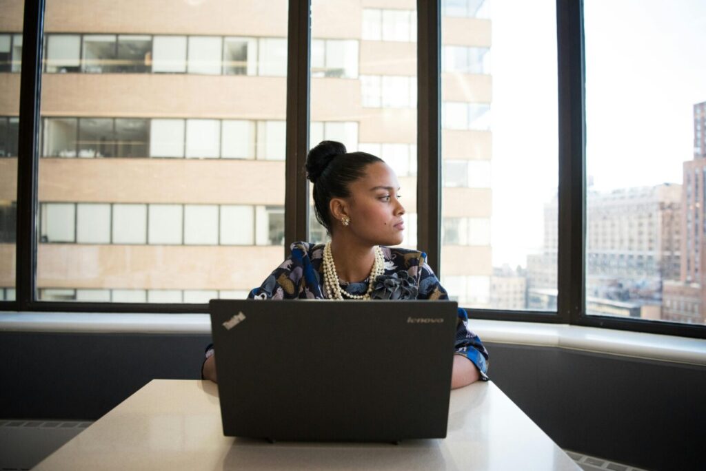 Confident woman working on a laptop in an office with large windows and city view.